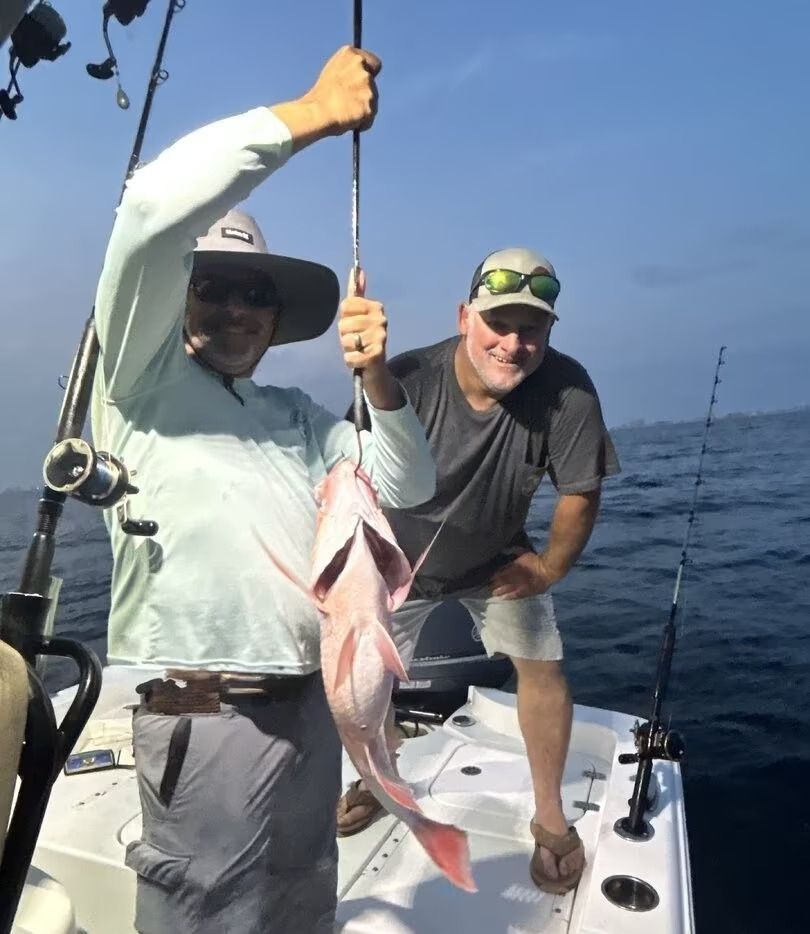 Two anglers on a boat holding up a freshly caught fish at sea