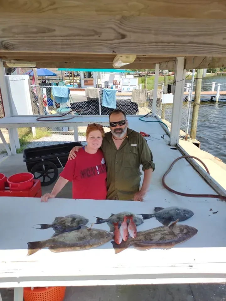 Two people posing at a dockside fish cleaning table with several fish laid out in front of them.