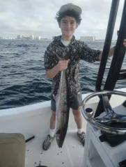 Person on a boat holding a large fish, with ocean waves and distant shoreline in the background.