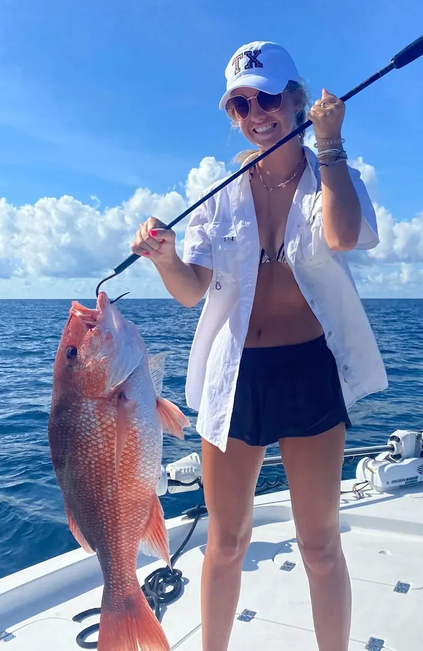Person on a boat holding a large red fish against a blue ocean and sky