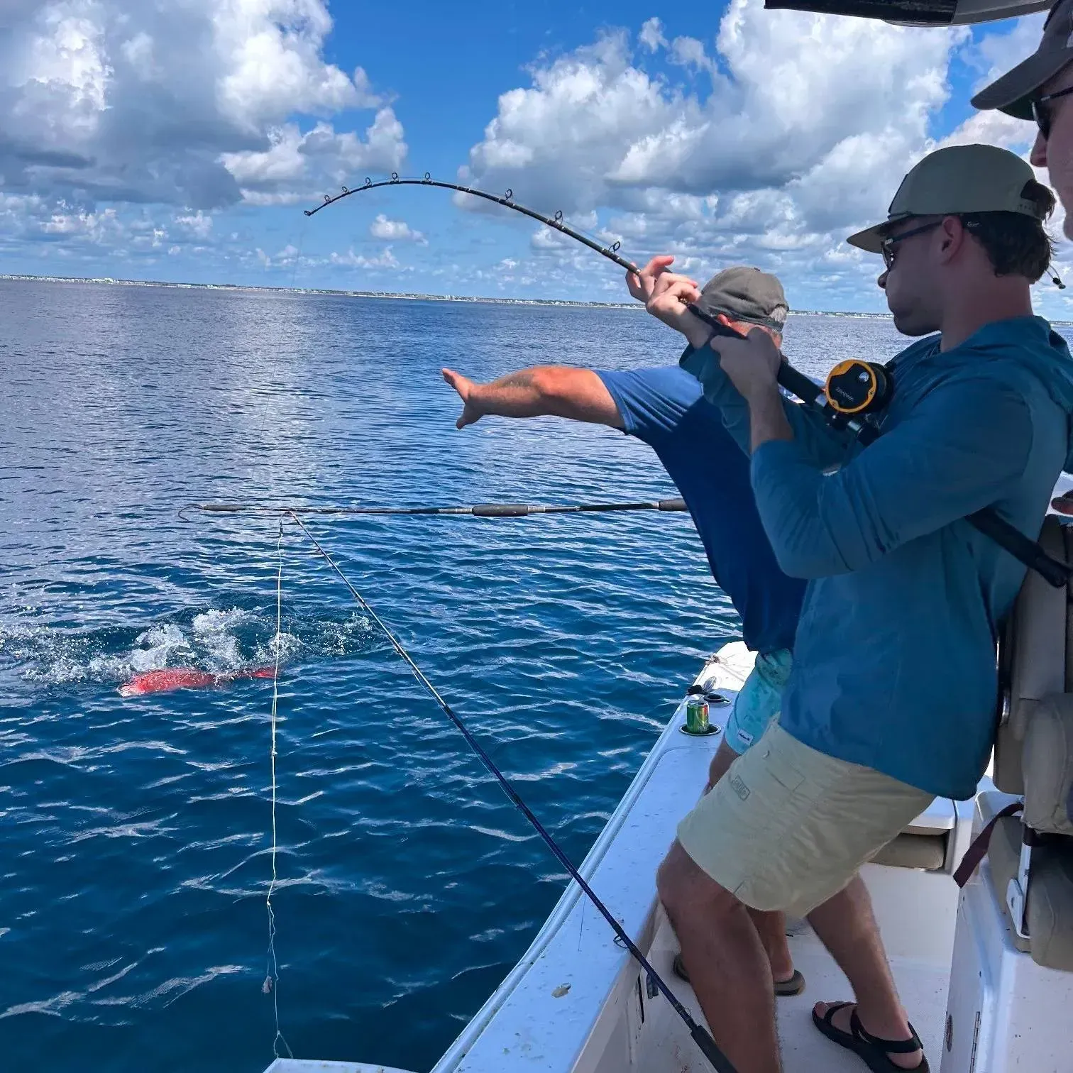 Two people fishing from a boat on blue open water under a cloudy sky