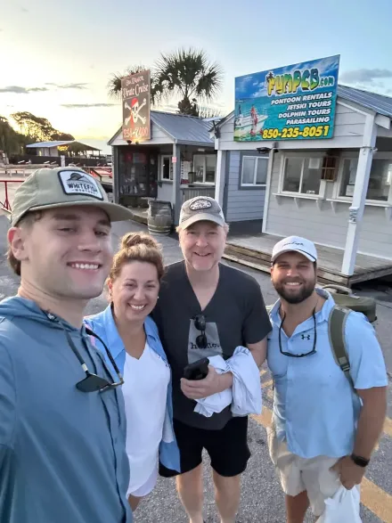 Four people smiling for a selfie outside a beachside shop at sunset.