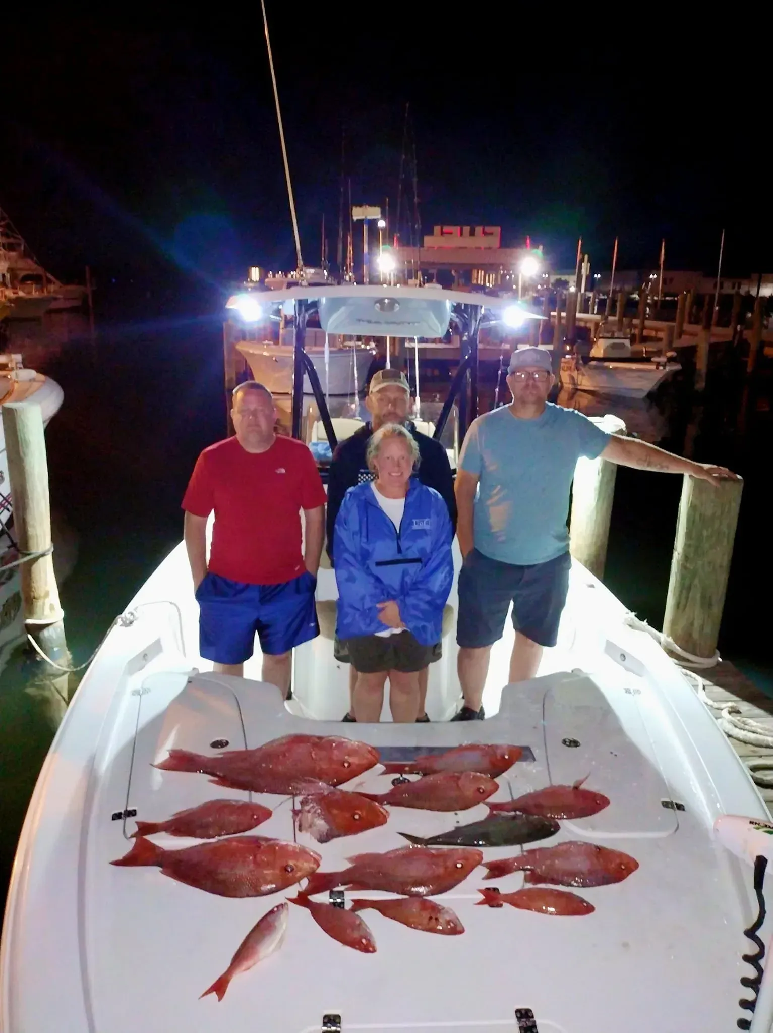 Three people on a boat at night posing beside a large catch of red fish on the deck