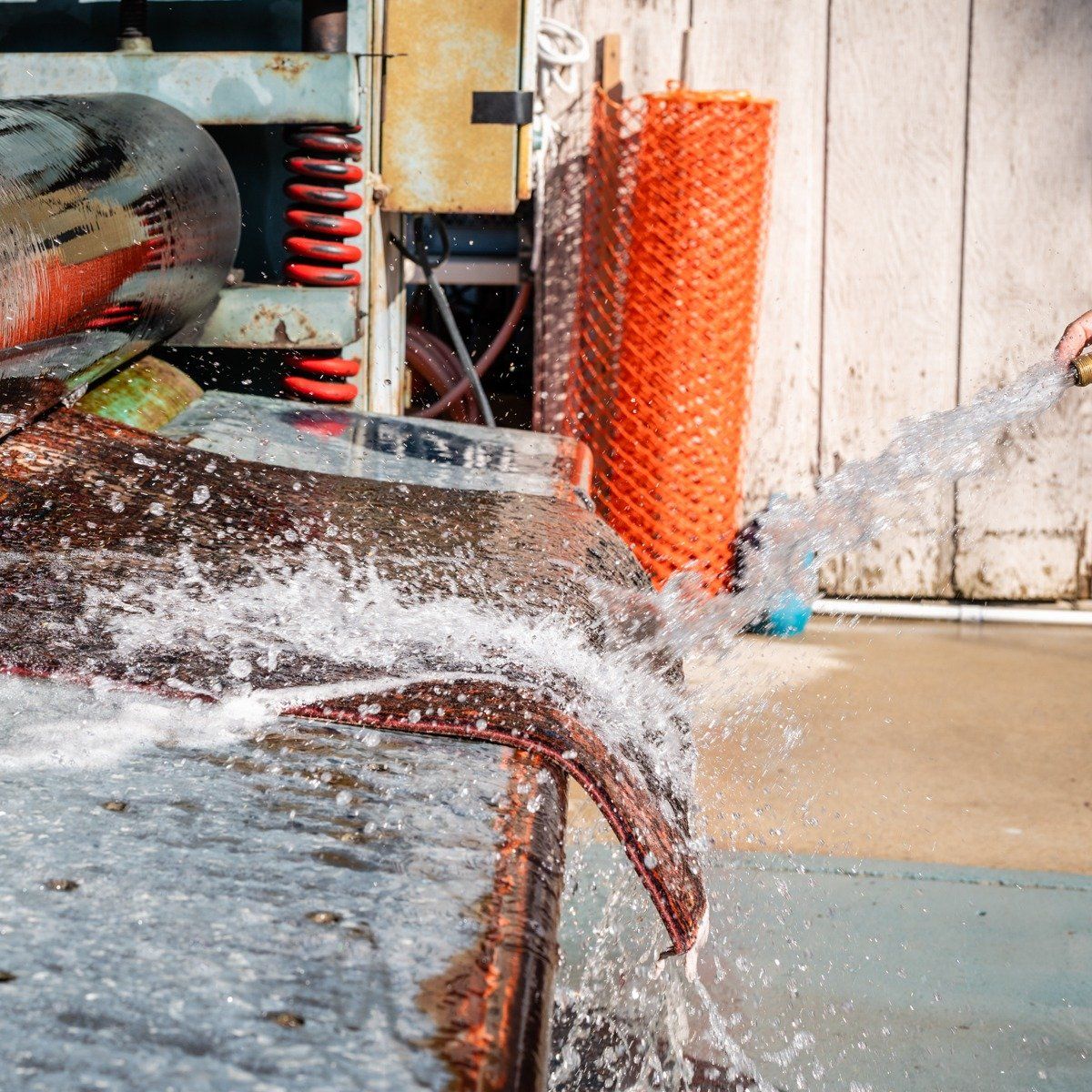 A stream of water from a hose washes off a rusted, metal industrial structure outdoors.
