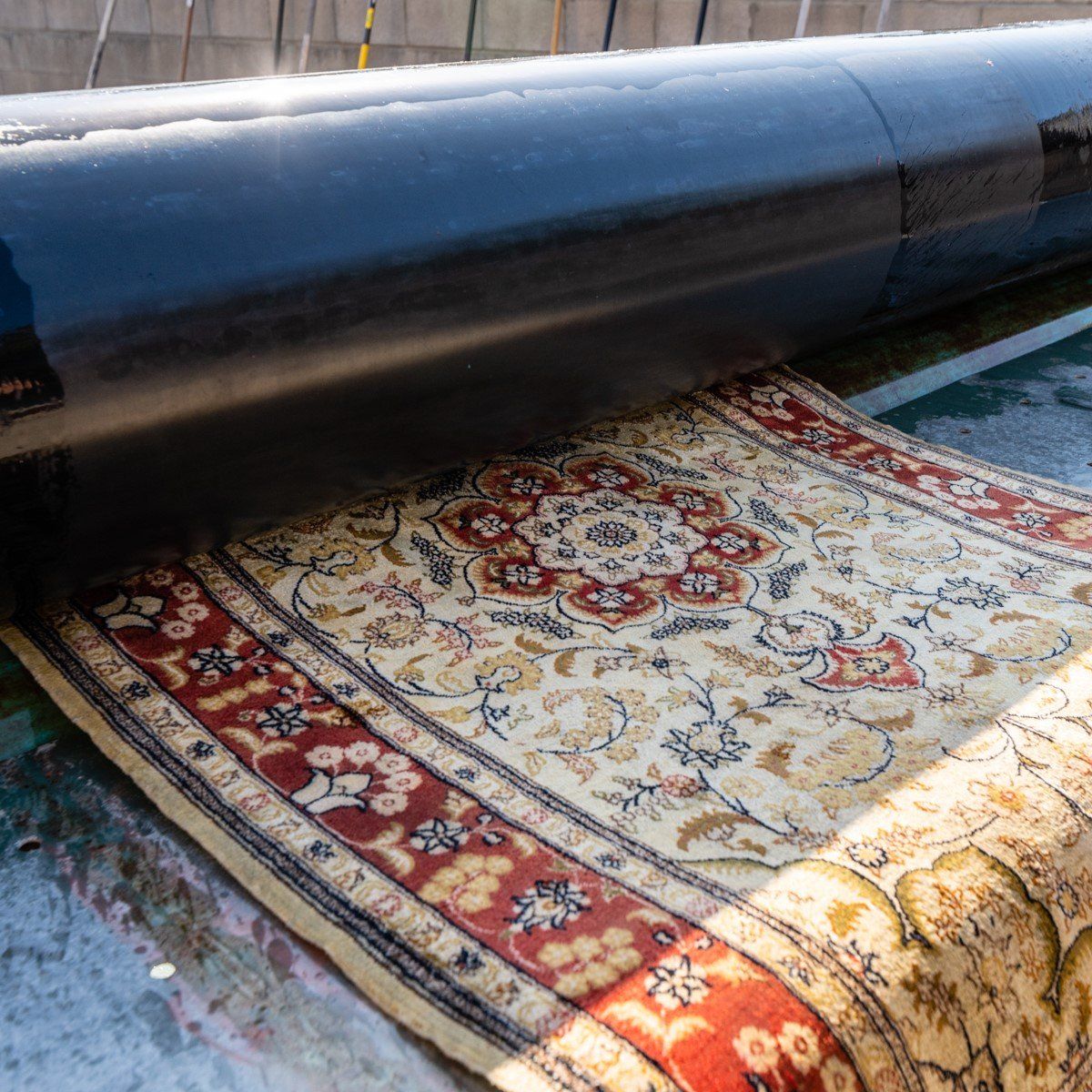 A patterned area rug being fed into a large industrial machine for cleaning.