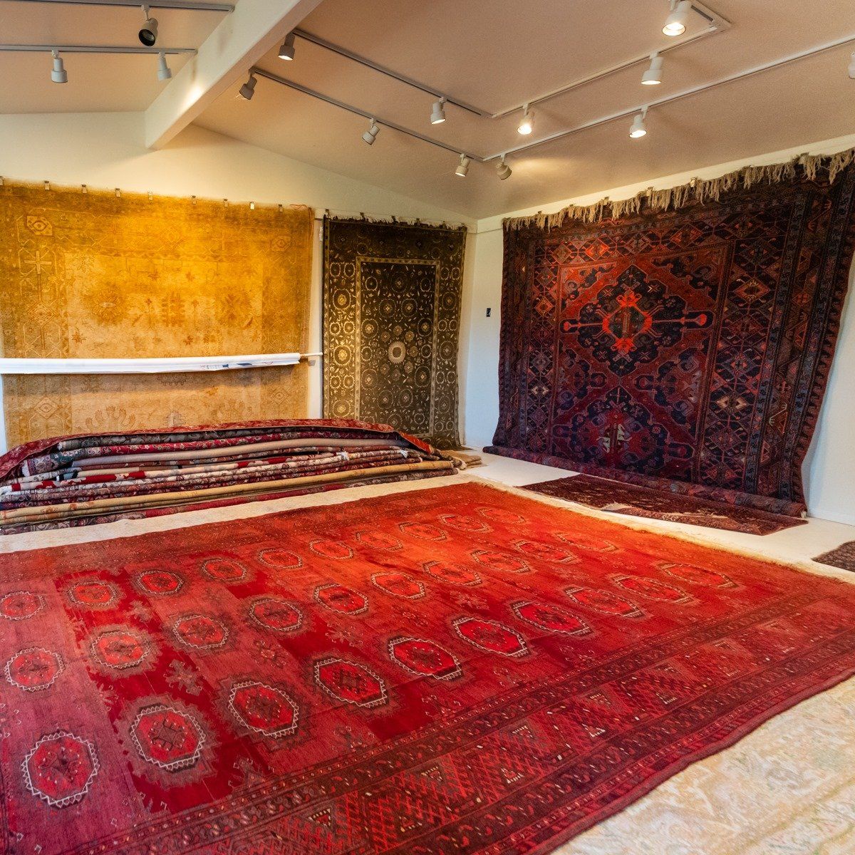 A rug showroom featuring a large red carpet in the foreground, with several other rugs displayed on the walls.
