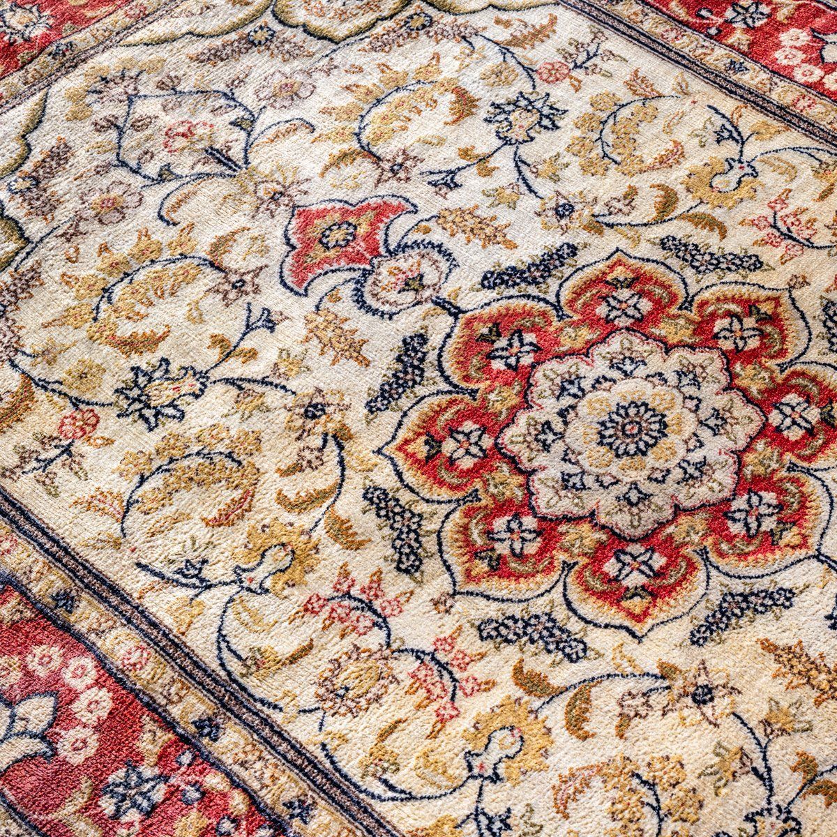 A close-up of a decorative rug featuring intricate red, blue, and gold floral patterns on a cream background.