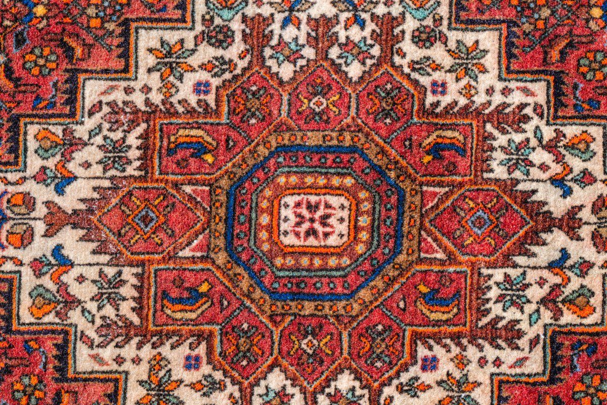 Intricate, symmetrical Persian rug pattern with a central octagonal motif in deep reds, blues, and creams.
