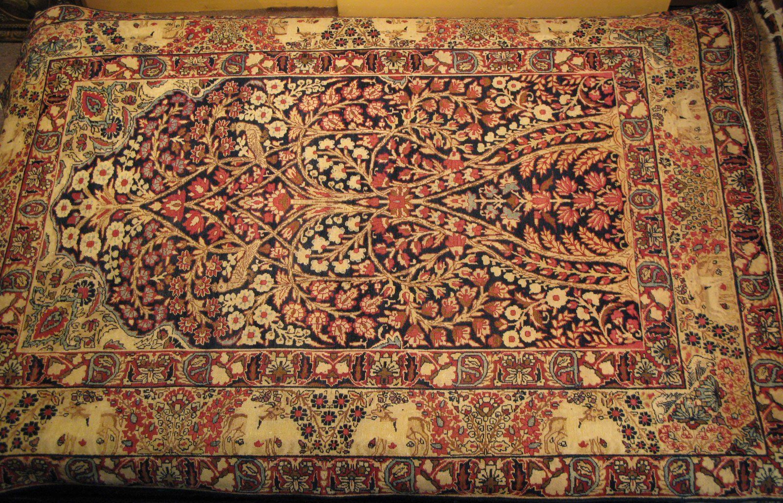 An ornate Persian rug with a central floral tree motif in shades of red, navy, and cream, framed by a deer-patterned border.
