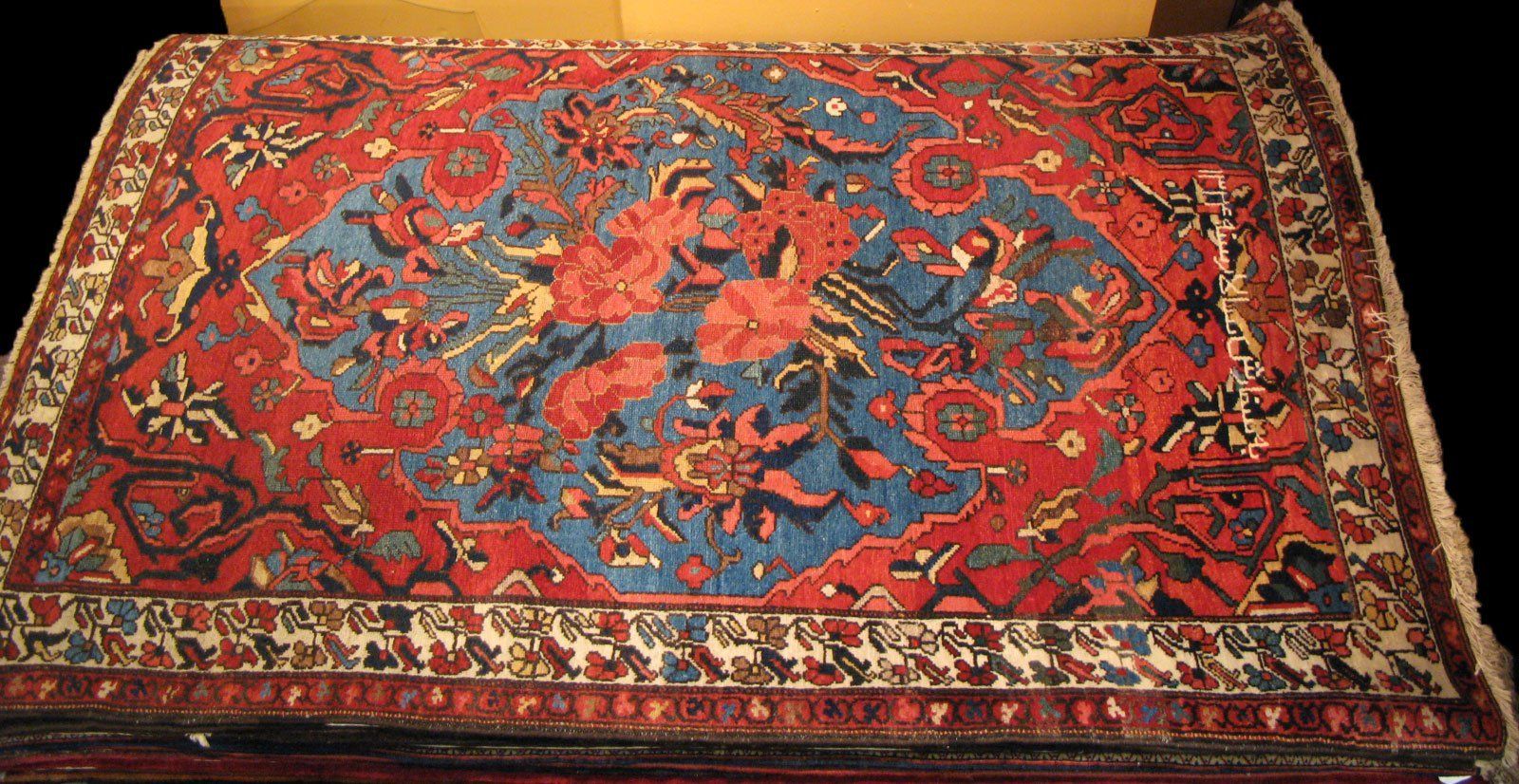 A rectangular rug featuring a blue central medallion with floral patterns on a red background and intricate borders.