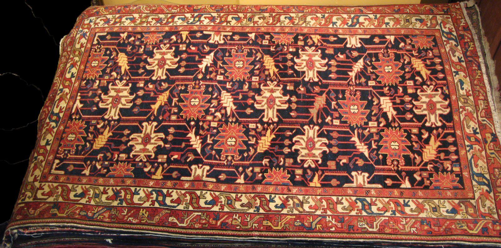 A rectangular rug with a dark field, repeating floral geometric motifs in red and cream, and a patterned border.