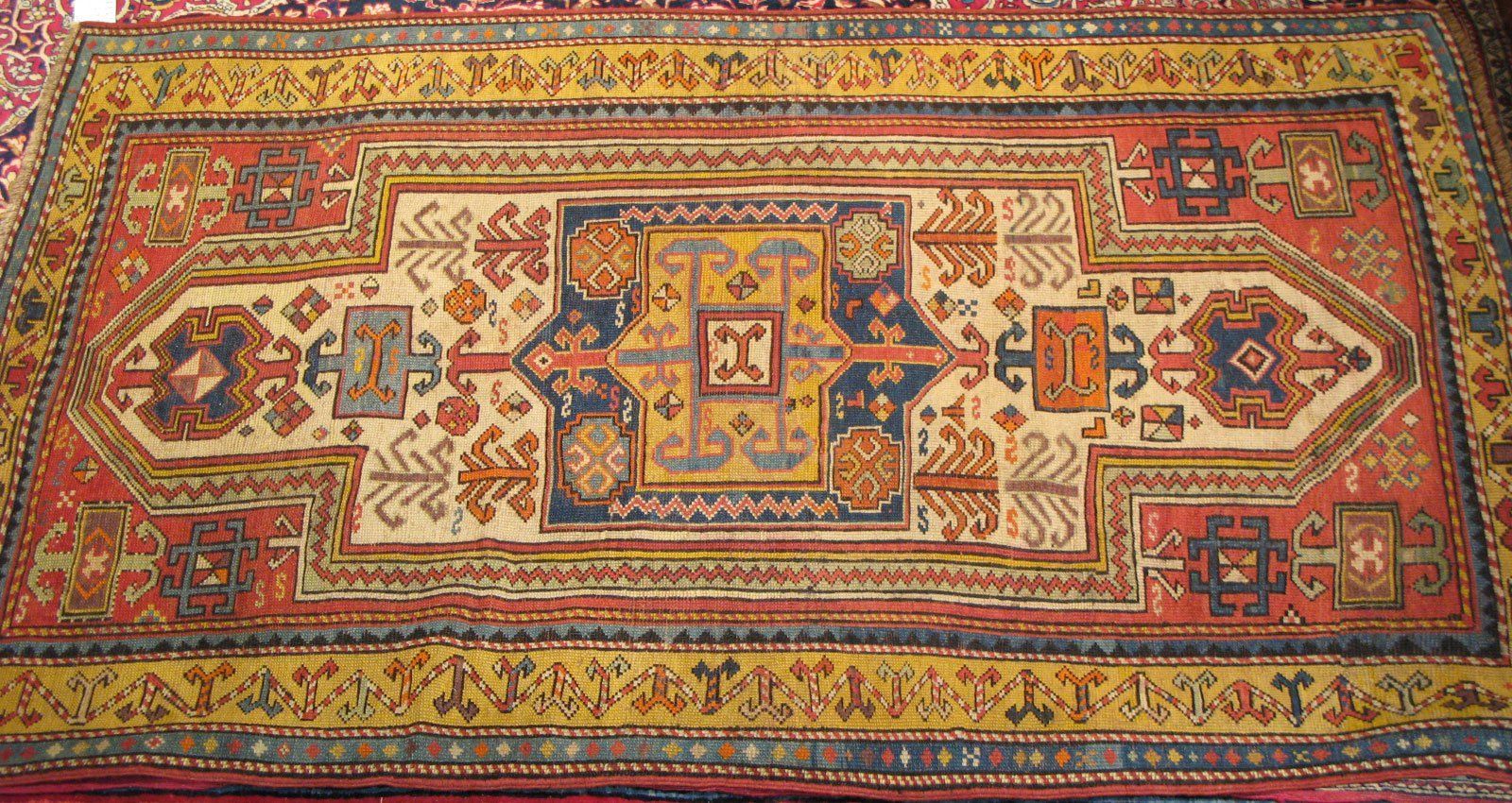 An ornate rectangular rug featuring a central geometric medallion, stylized floral motifs, and a patterned yellow border.