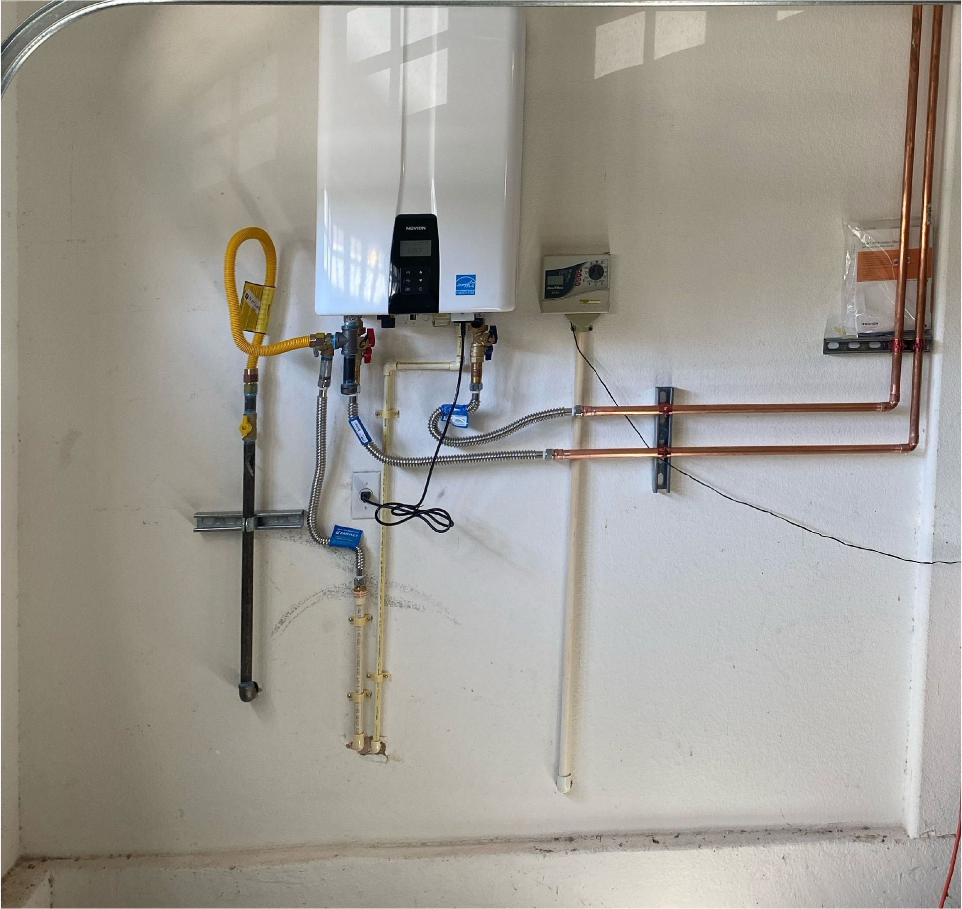 A white wall with copper pipes and a water heater