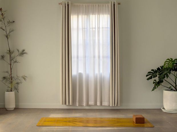 A golden yoga mat and cork block laid out on the concrete floor at Yoga Shala Collective, beside a curtained window and potted plants