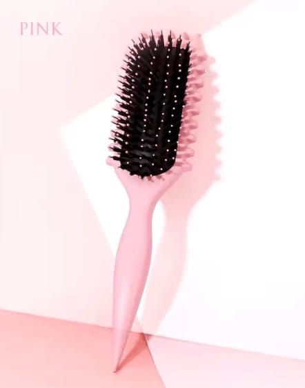 Un cepillo rosa con cerdas negras se alza erguido sobre un fondo dividido en rosa y blanco.