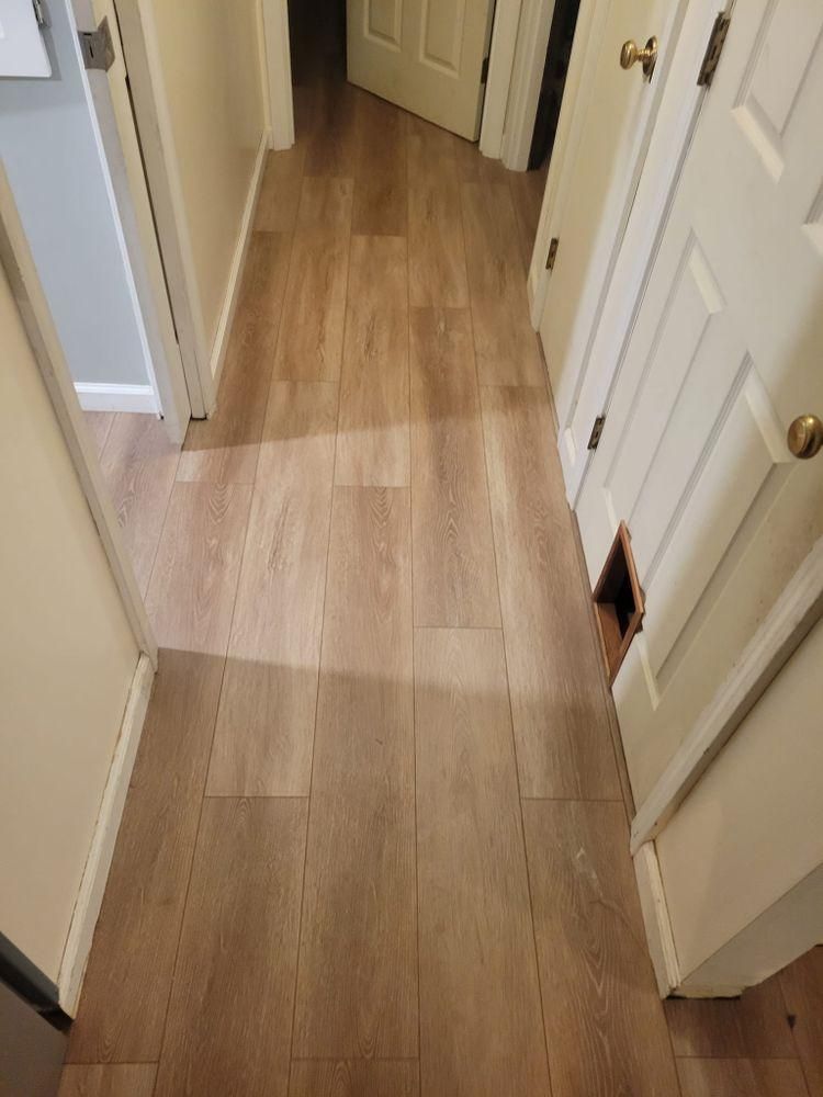 Narrow hallway with light wood flooring, white doors, and a damaged patch near the right door frame