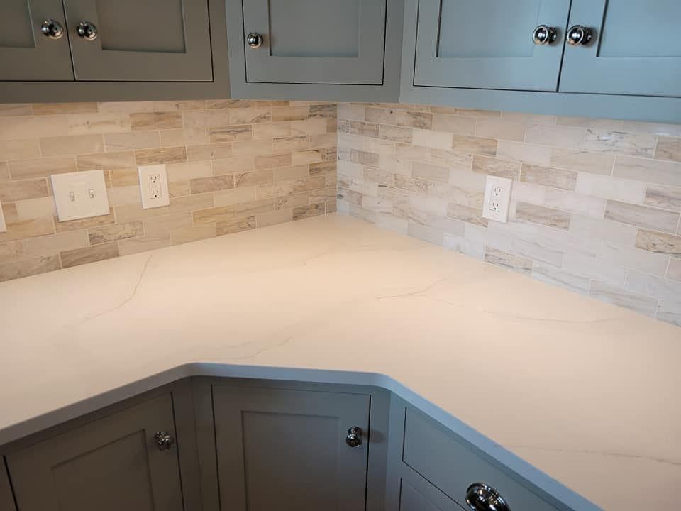 Corner kitchen countertop with light stone backsplash and gray cabinets above and below.