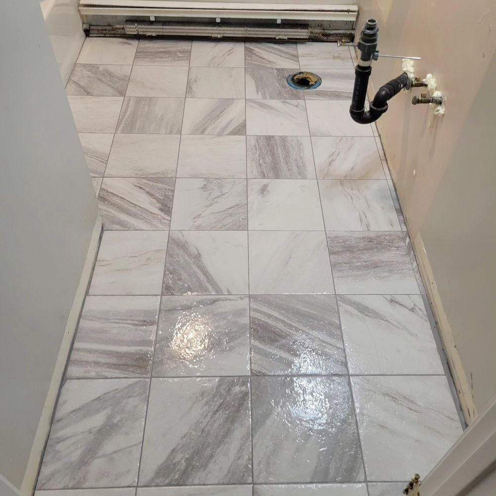 Empty tiled laundry or utility room floor with a drain and exposed plumbing on the right.