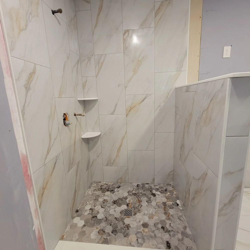 Empty tiled shower stall with marble-look walls, pebble floor, and built-in corner shelves.