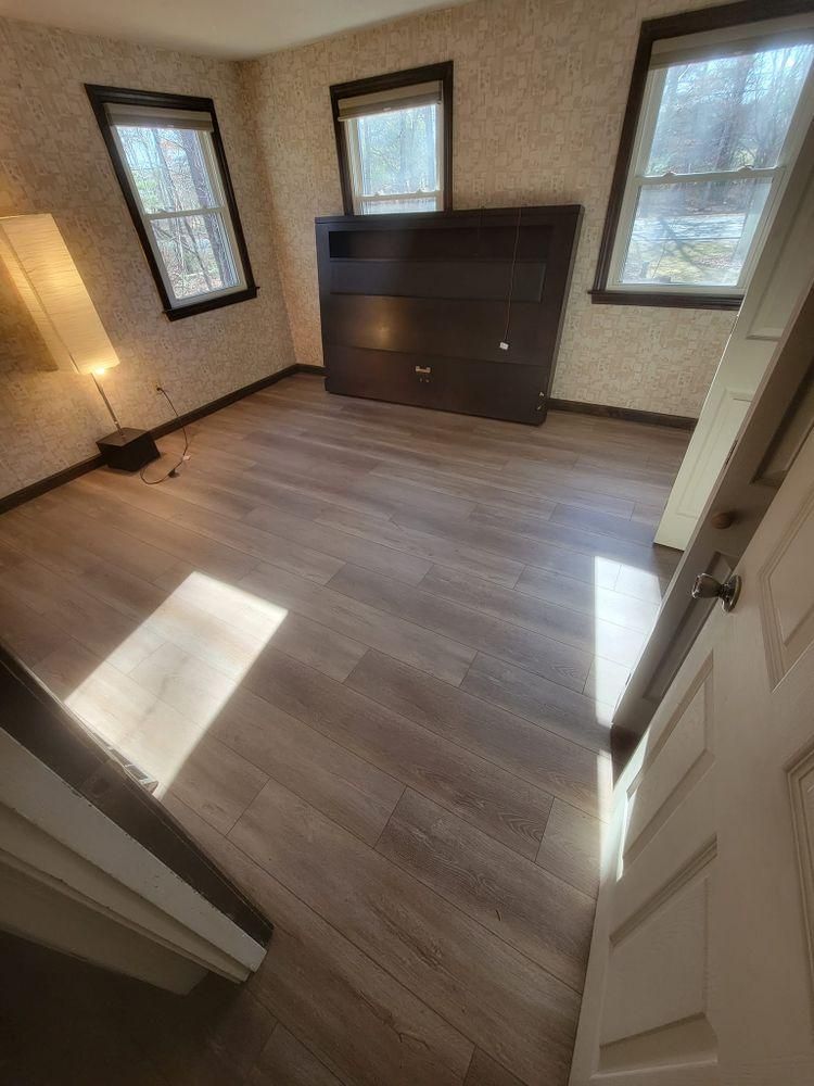 Empty room with wood flooring, three windows, and a dark fireplace mantel