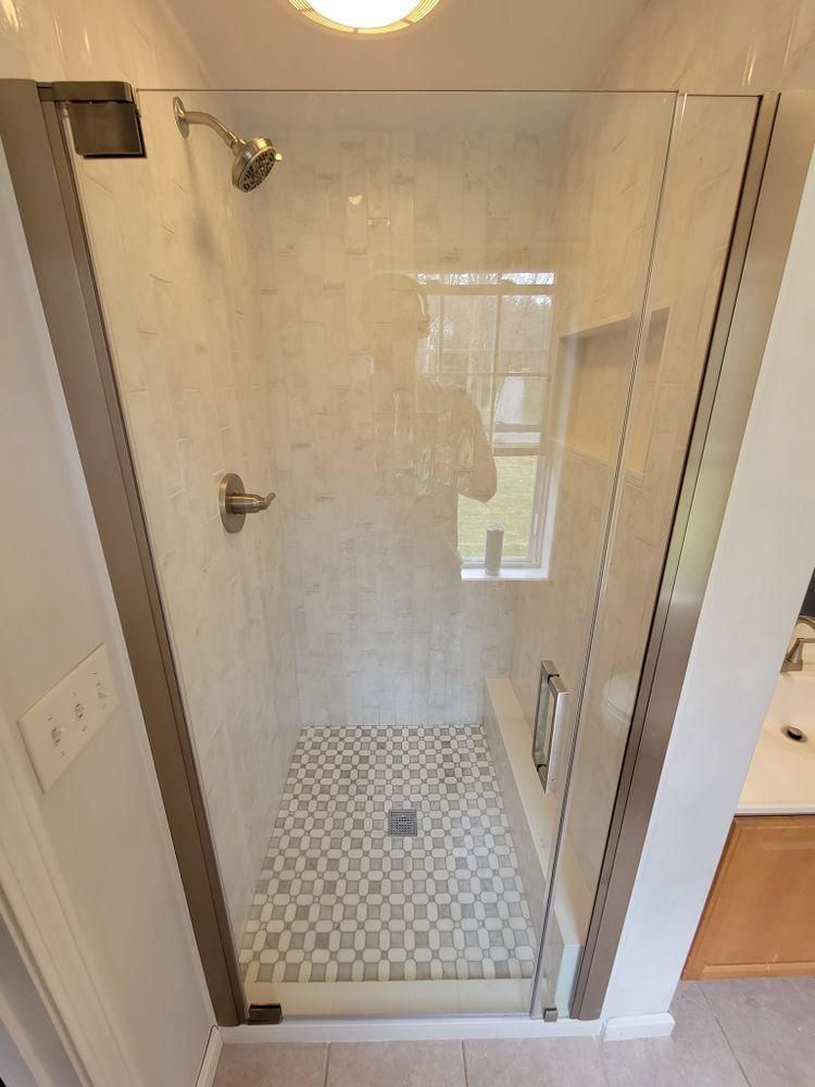 Glass walk-in shower with chrome fixtures and patterned tile floor in a bathroom