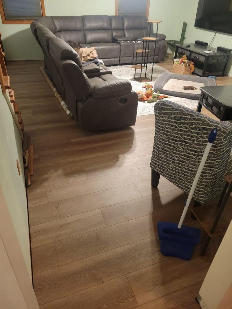 Living room with gray sectional sofa, coffee table, wicker chair, and broom on wood floor