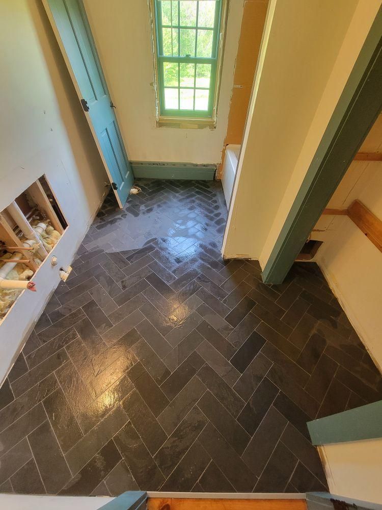 Stairwell with dark herringbone tile floor and a window letting in green light