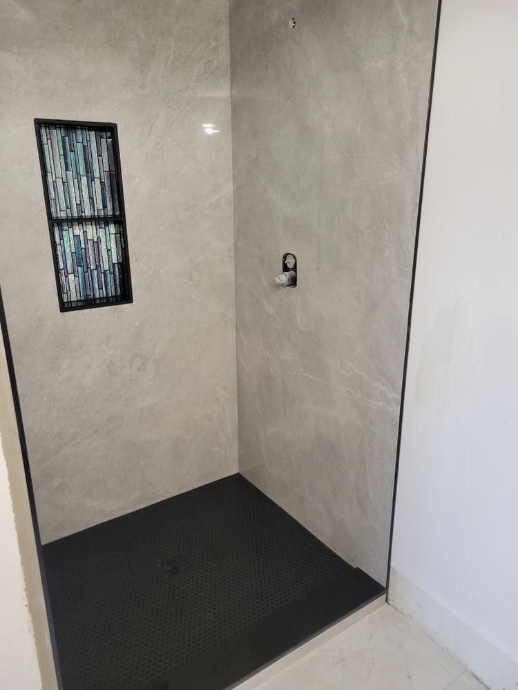 Small tiled shower stall with black floor, light gray walls, and a narrow window.