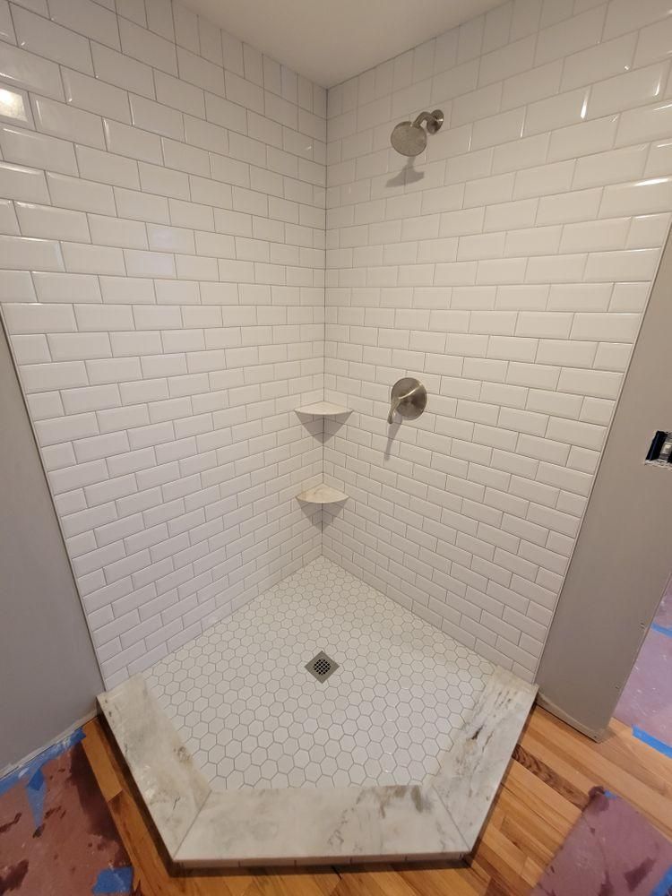 White-tiled walk-in shower with corner shelf, showerhead, and small hexagonal floor.