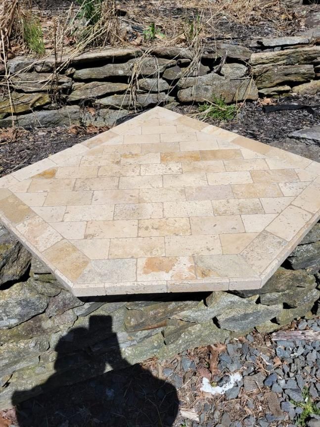 Hexagonal beige stone patio table on a rocky outdoor slope, with a stone wall behind it.