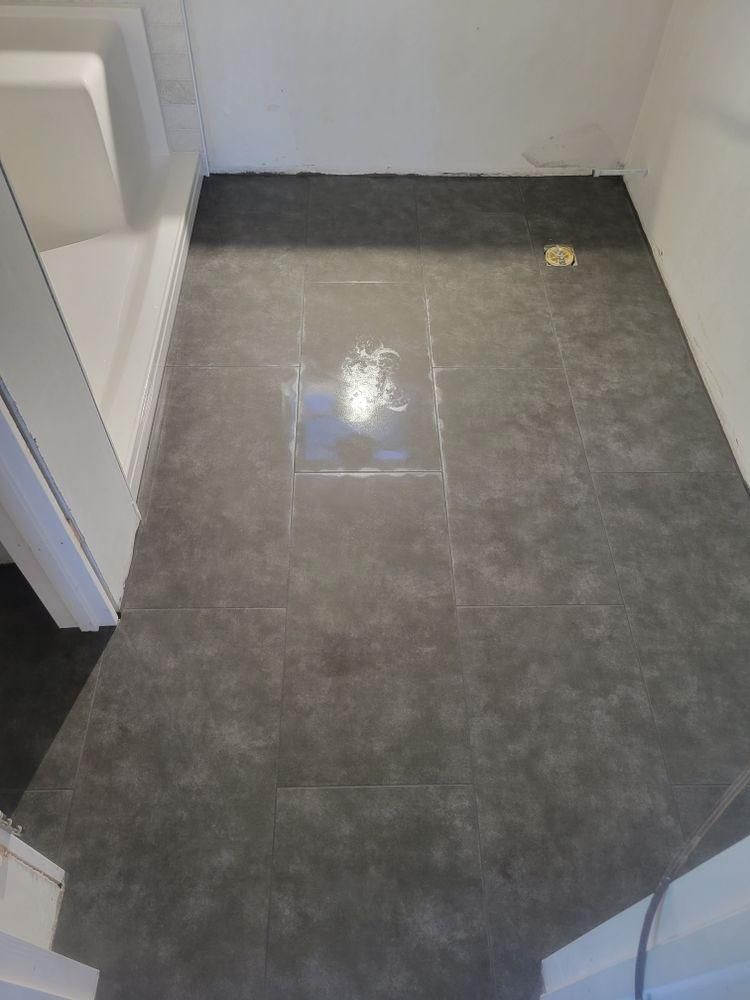 Small tiled bathroom or hallway floor with dark gray tiles and white walls, viewed from a doorway.