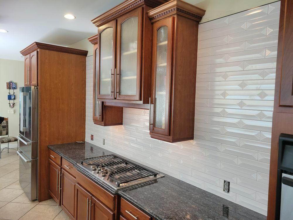 Modern kitchen with dark wood cabinets, granite counters, stainless refrigerator, and tiled backsplash.
