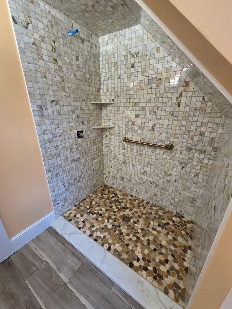Tiled walk-in shower with mosaic floor, built-in shelf, and sloped ceiling.