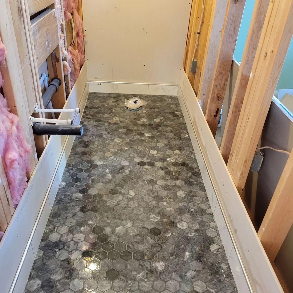 Narrow unfinished bathroom with tiled floor, exposed wall framing, and plumbing during renovation