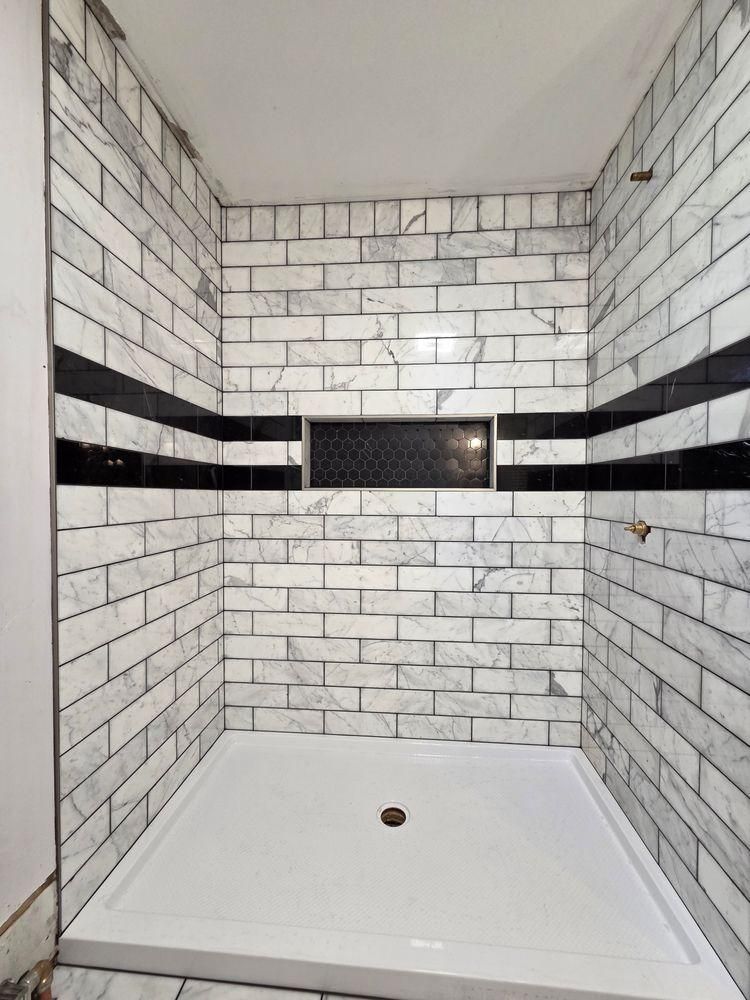 Empty tiled shower with white brick walls, black accent band, and white shower base.