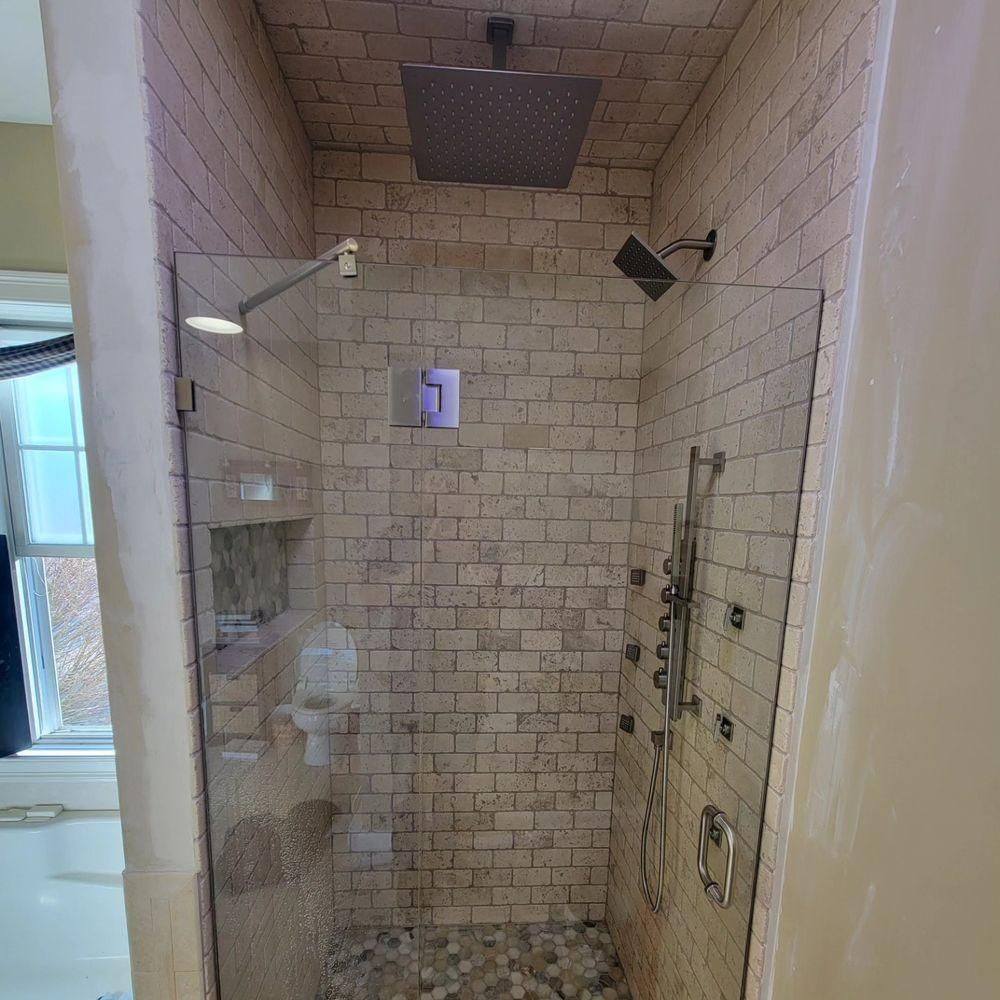Tiled walk-in shower with glass door, rainfall showerhead, and built-in shelves.
