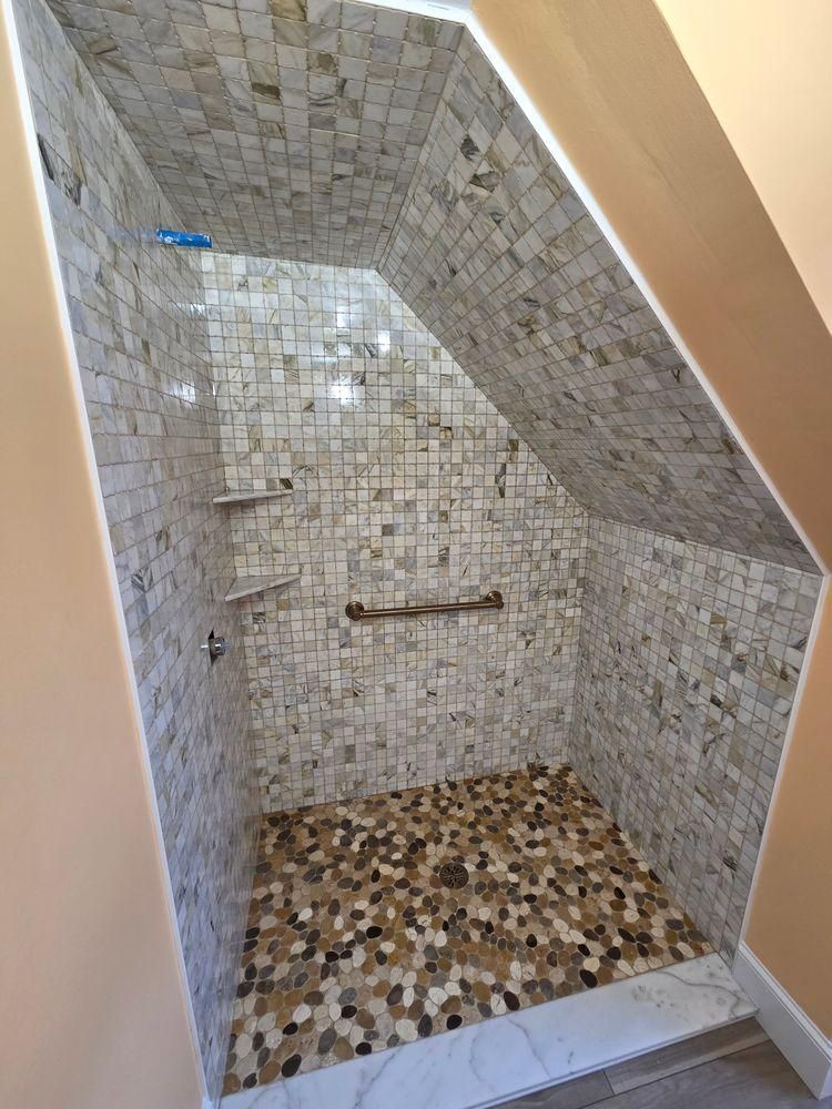 Small tiled shower stall with a built-in bench and pebble-style floor.