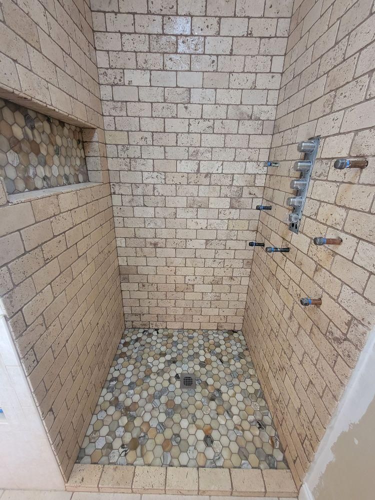 Small tiled shower stall with pebble floor, wall fixtures, and unfinished edges.