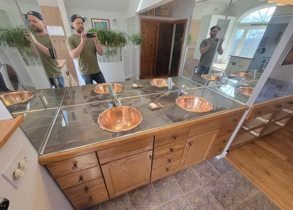 Mirrored bathroom vanity with copper sinks and a person reflected taking a selfie