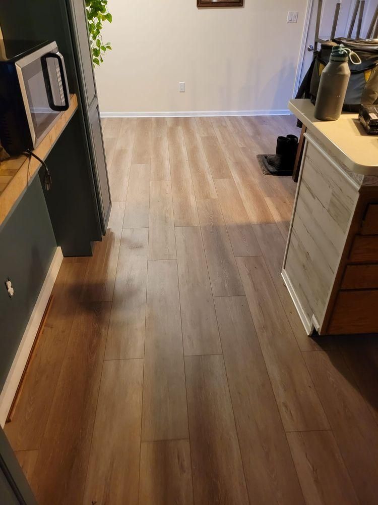 Narrow kitchen aisle with wood floors, dark cabinets, and light countertops leading to a back wall.