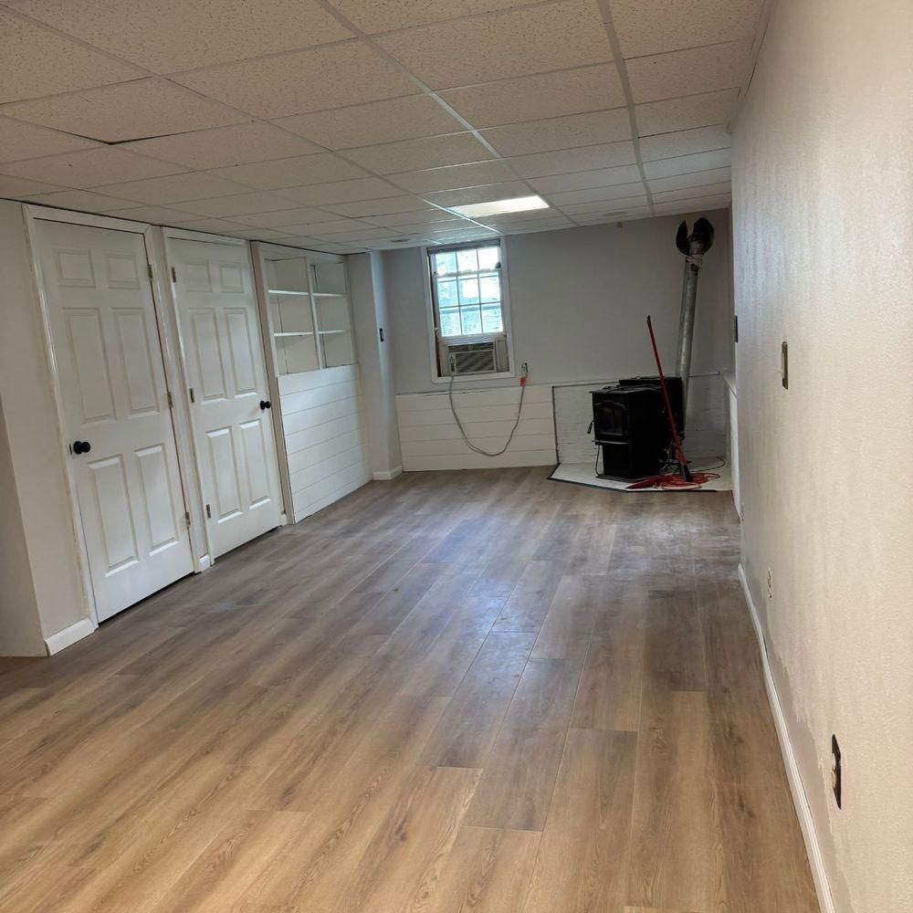 Empty room with light wood flooring, white walls, closet doors, and a small window at the far end.