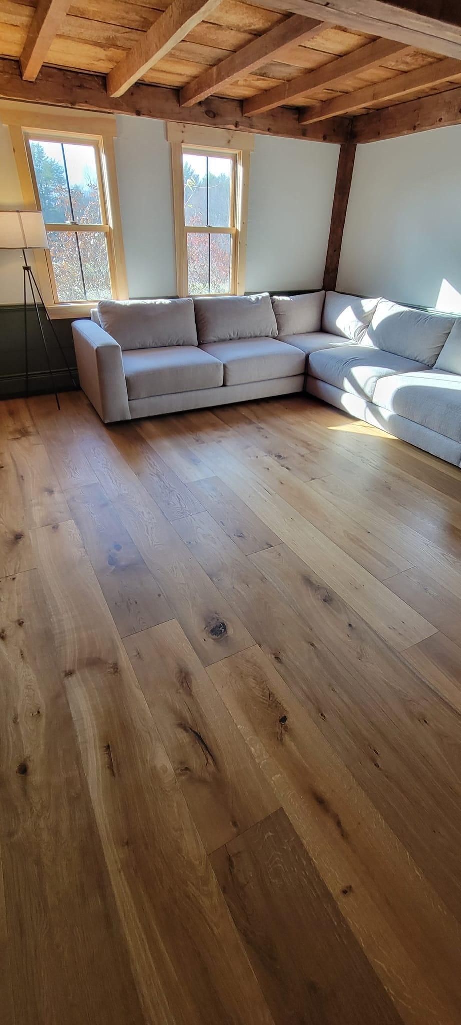 Sunlit living room with light wood floors, white sofa, and exposed wooden ceiling beams