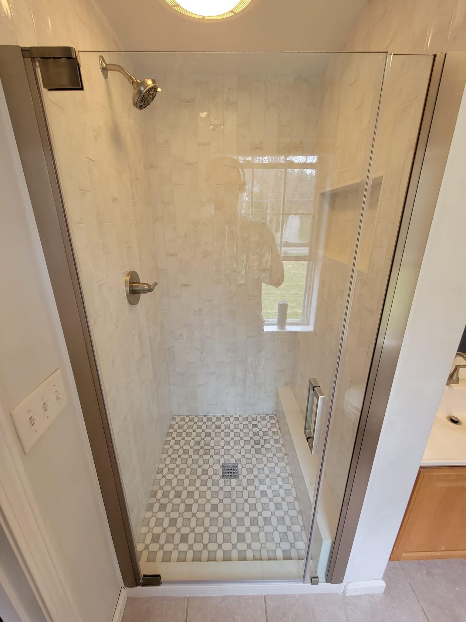 Empty glass shower stall with white tile floor and a wall-mounted showerhead in a bathroom.