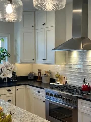 Modern white kitchen with stainless steel stove, hood, and pendant lights
