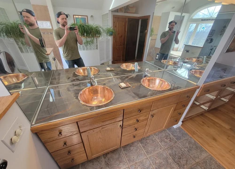 Bathroom vanity with copper sinks, granite countertop, and large mirror reflecting two people taking a selfie