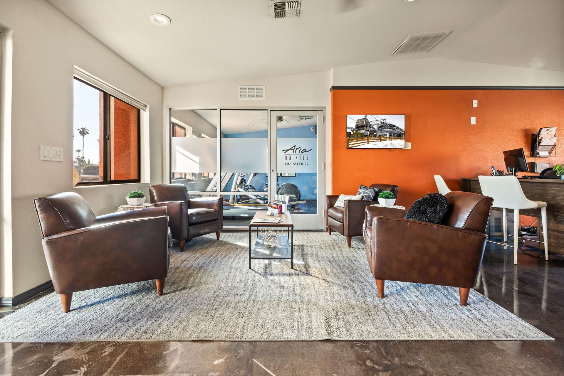 Lounge area with brown leather armchairs, rug, glass coffee table, and orange accent wall.