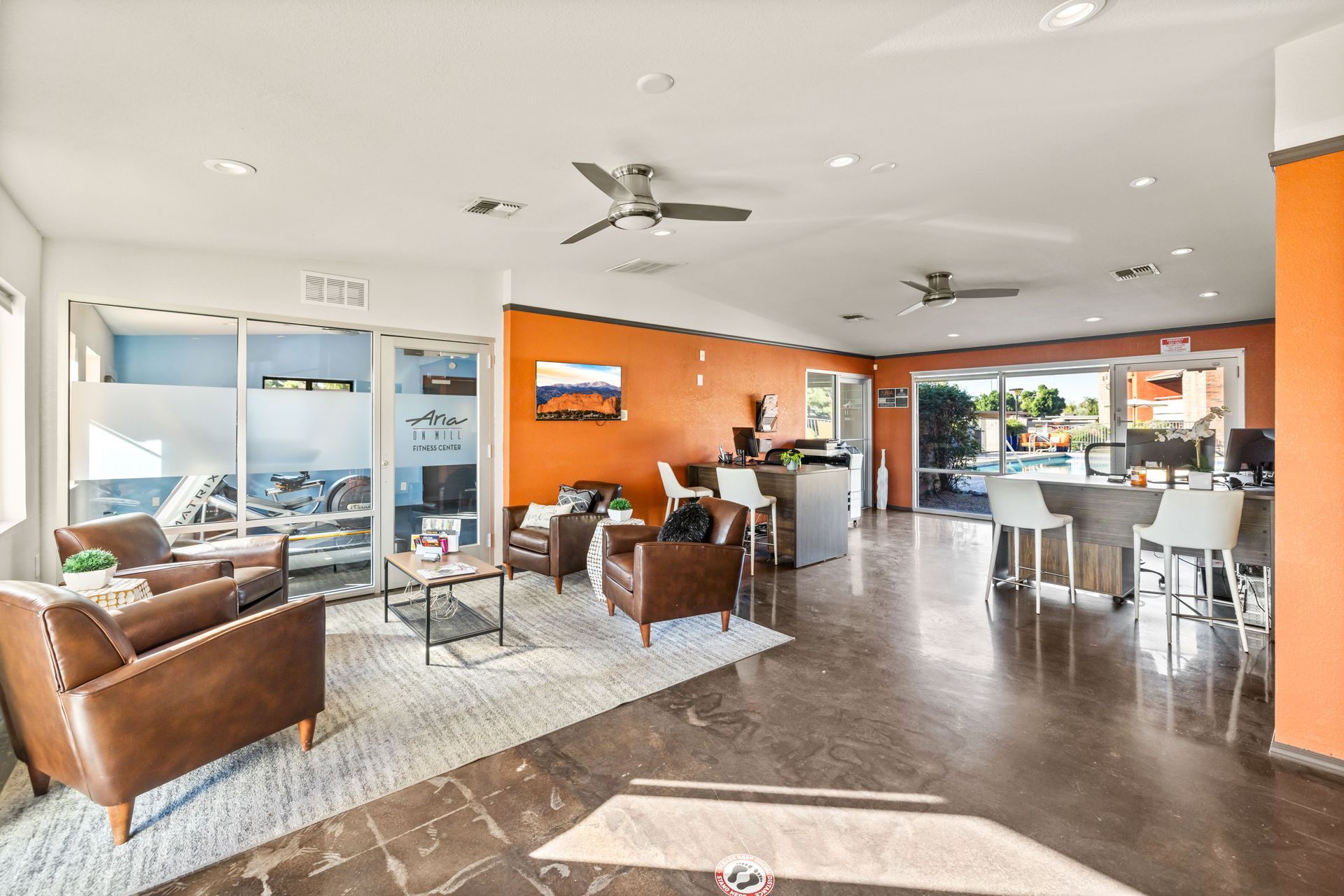Lounge area with brown leather chairs, orange accent wall, white rug, and bar seating.