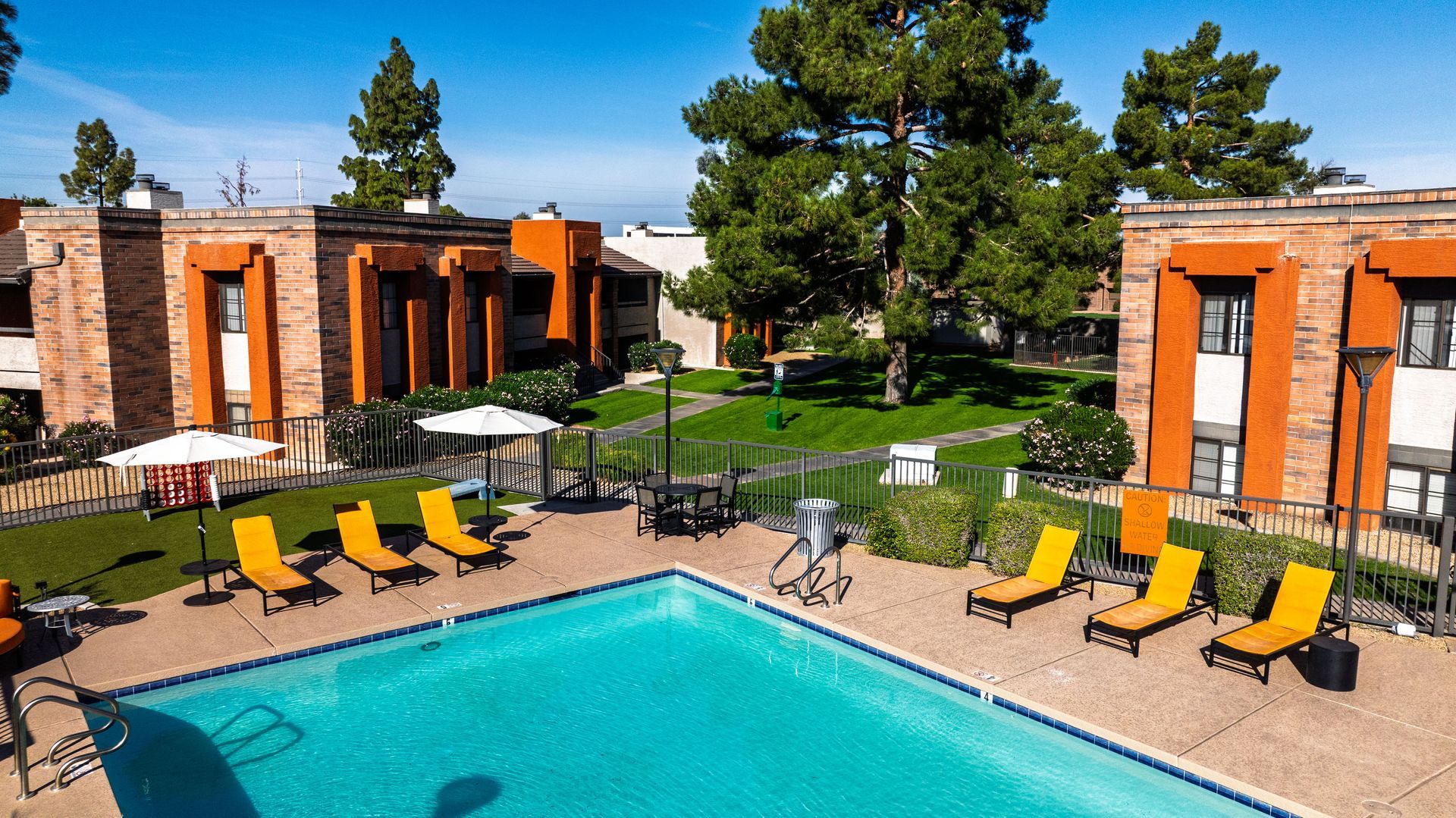 Modern courtyard with a turquoise pool, yellow lounge chairs, and brick buildings under a blue sky