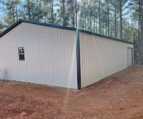 A large white building with a black roof is sitting in the middle of a dirt field.