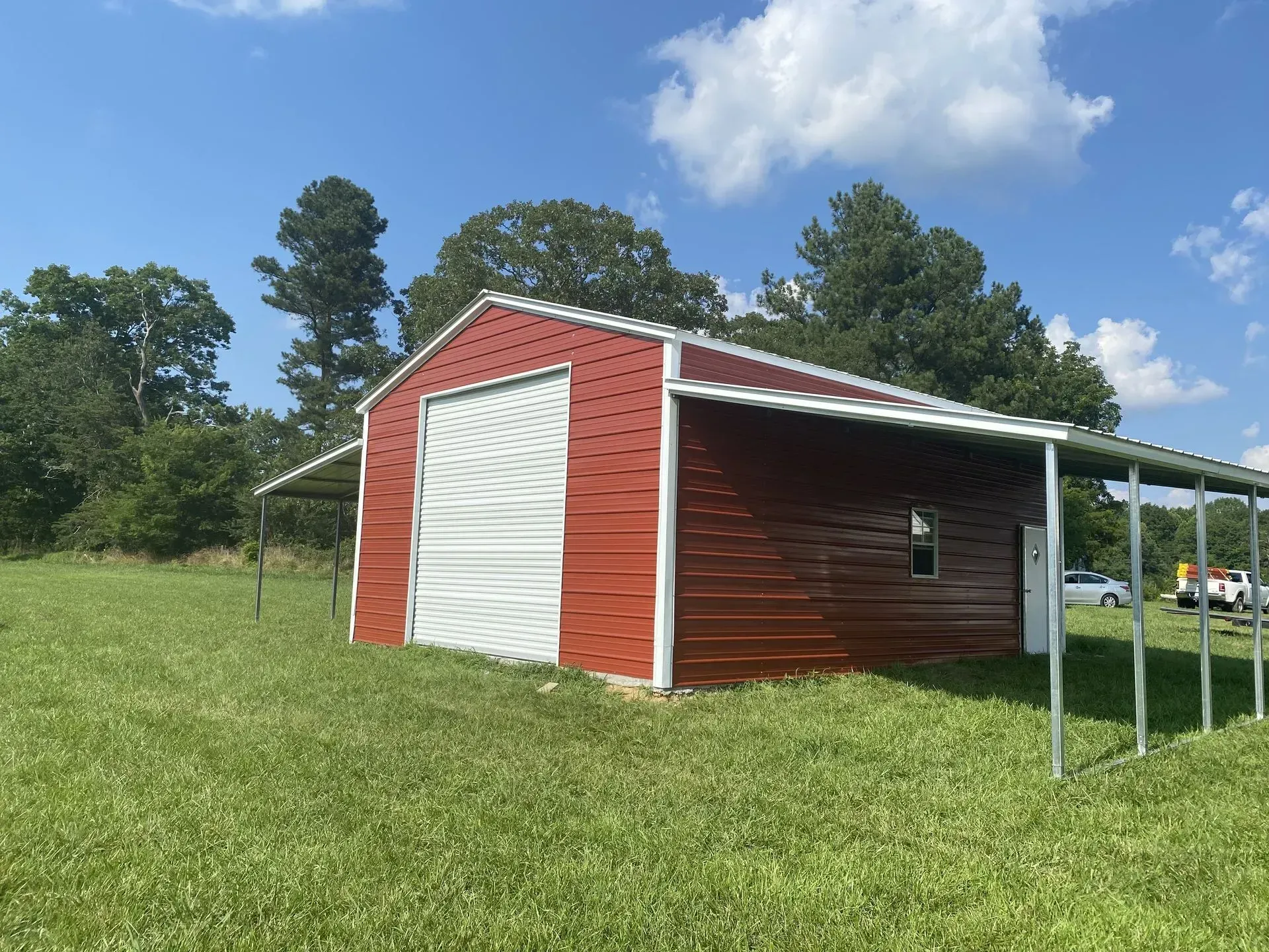 A red barn with a white door is sitting in the middle of a grassy field.